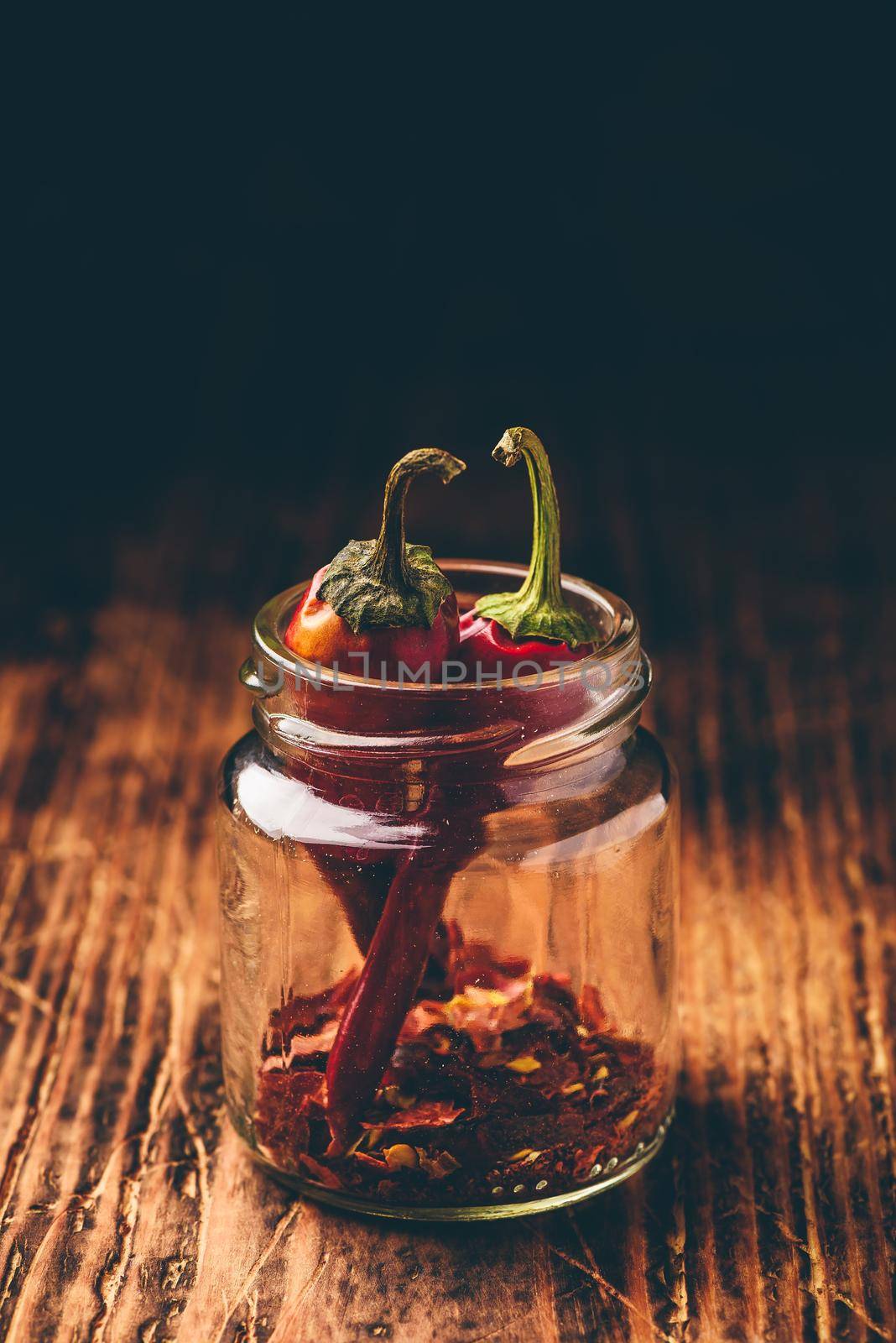 Two dried red chili peppers in jar with ground peppers