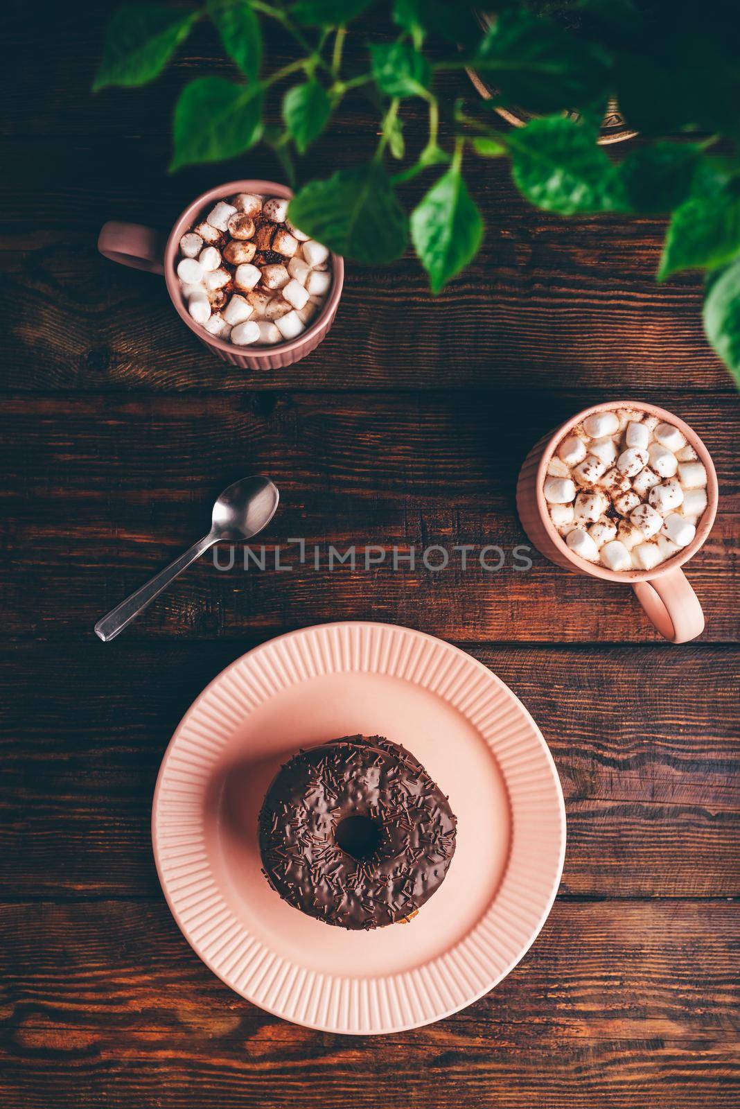 Stack of Homemade Chocolate Donuts and Mugs of Hot Chocolate with Marshmallow on Rustic Wooden Surface. View from Above