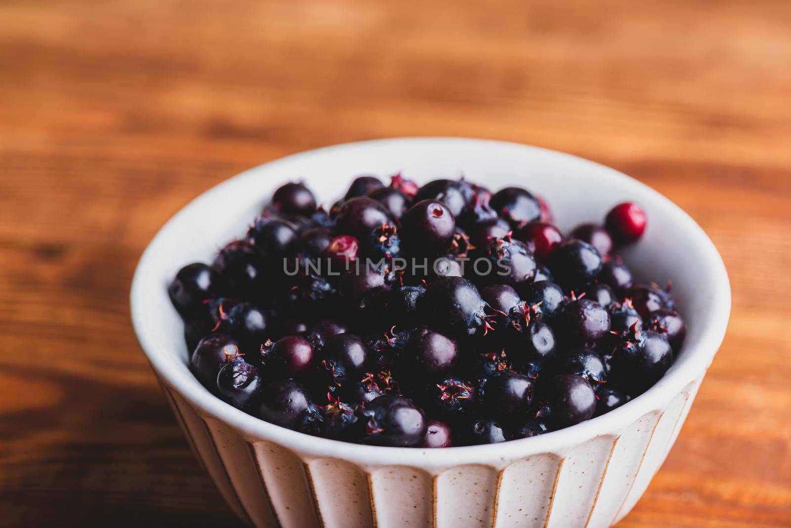 Bowl Full of Purple Amelanchier Lamarckii Fruits on Rustic Wooden Surface