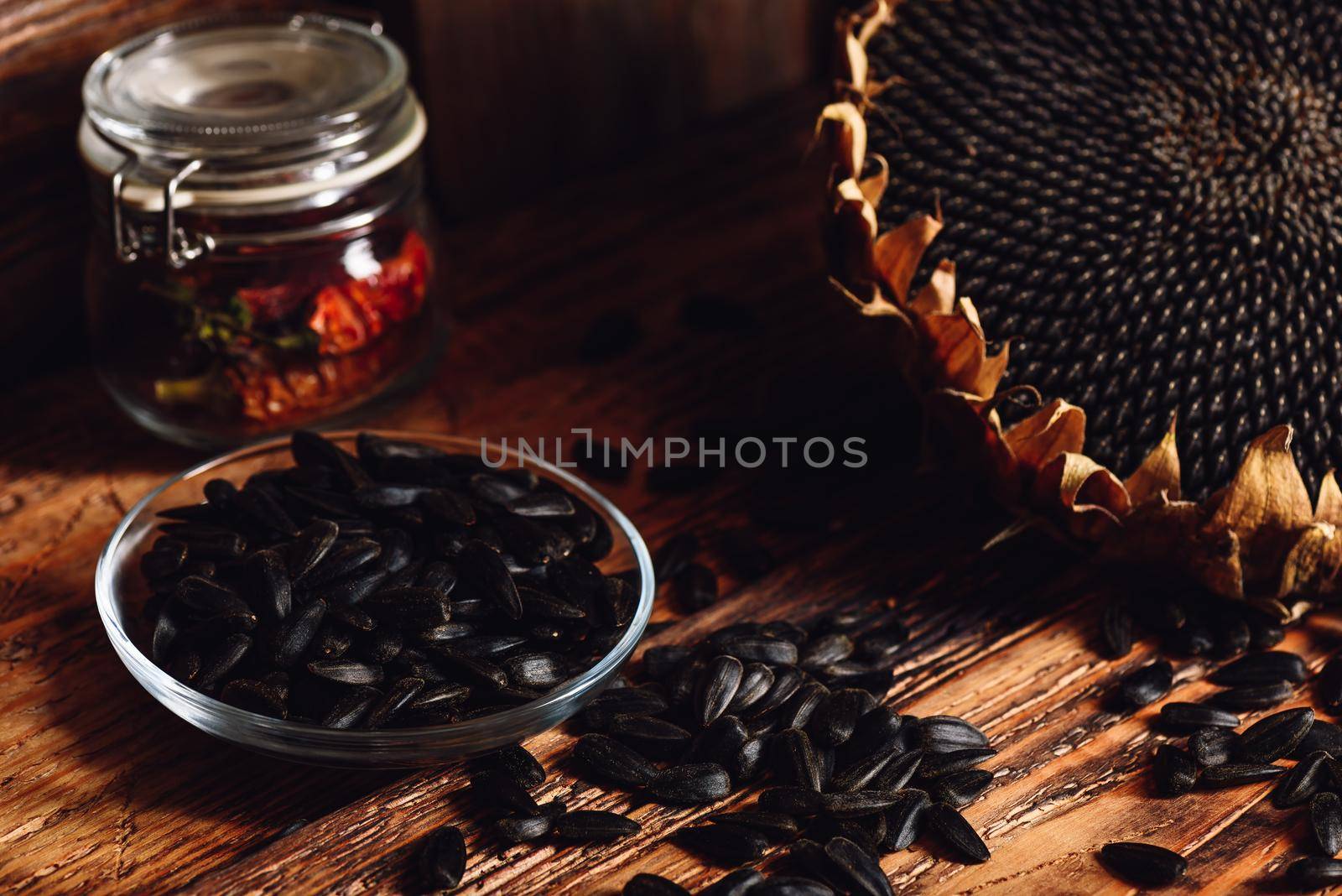 Roasted seeds on the glass saucer and dried sunflower over old wooden surface