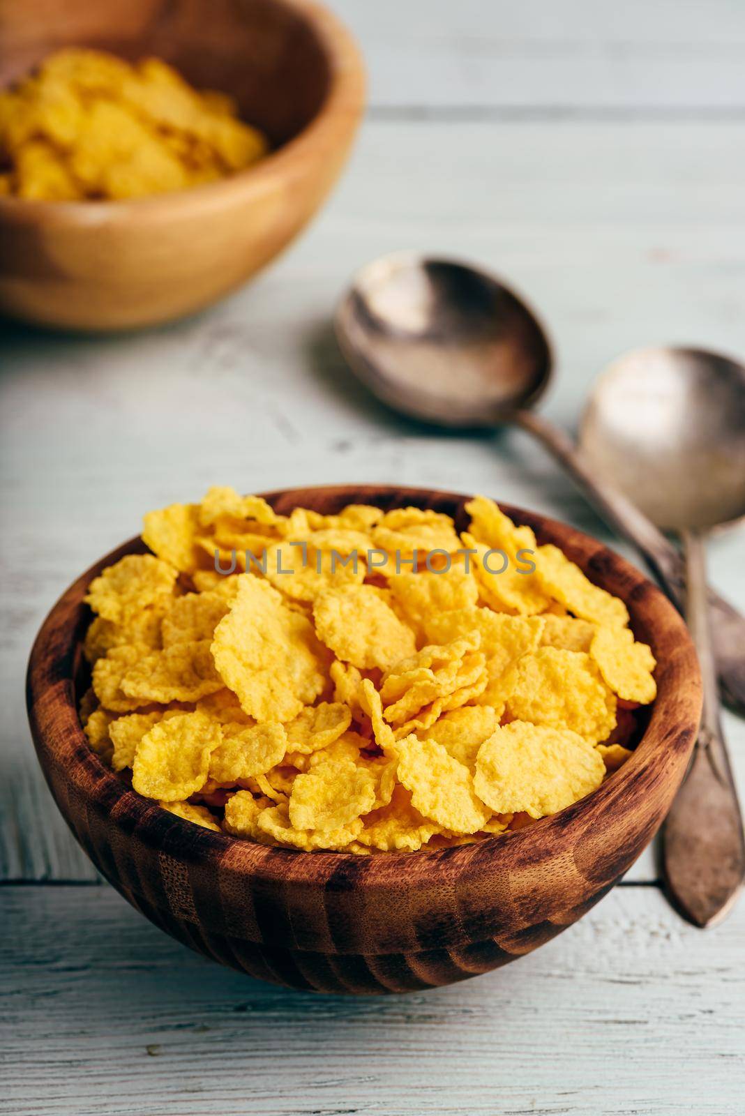 Rustic bowls of cornflakes with spoons on light wooden surface