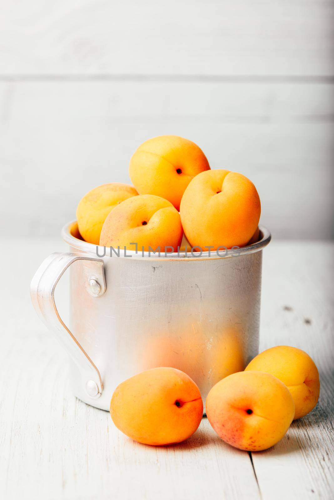 Mellow apricots in metal mug over light wooden surface