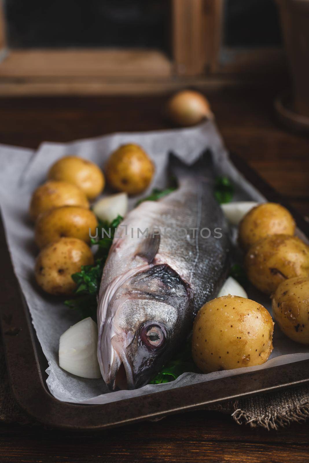 Fresh Fish Stuffed with Sorrel on Baking Sheet Being Prepared with New Potatoes and Onion