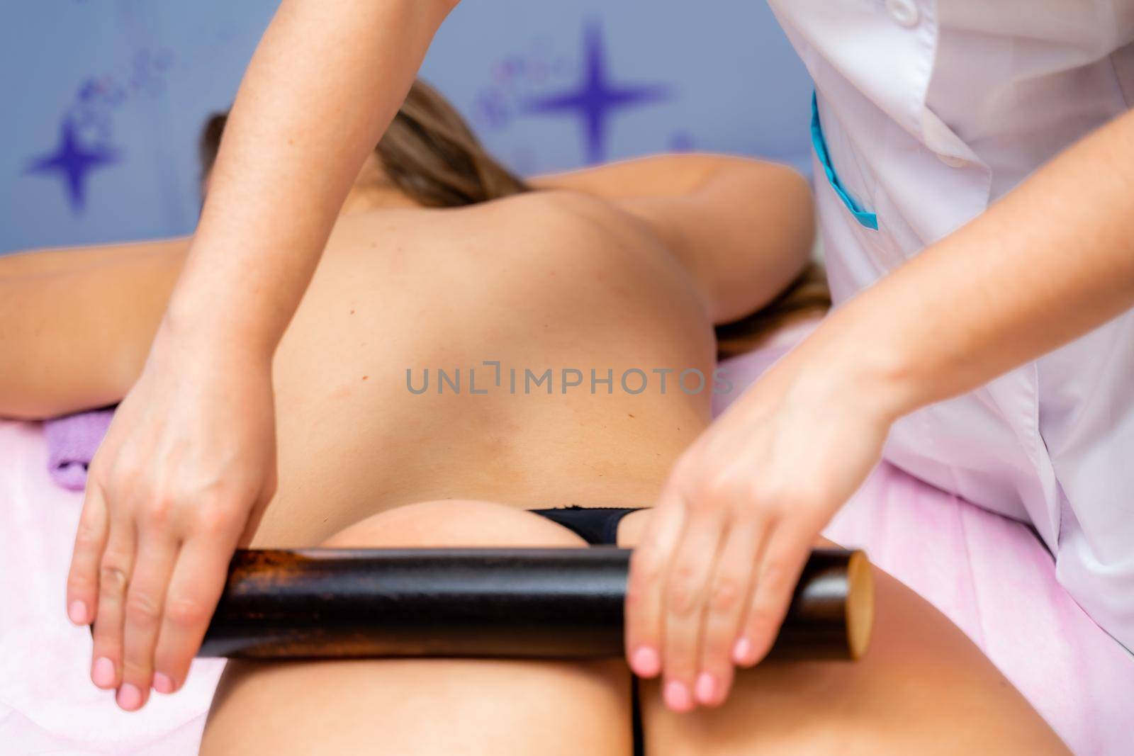 Woman having massage with bamboo stick in wellness center. by Matiunina