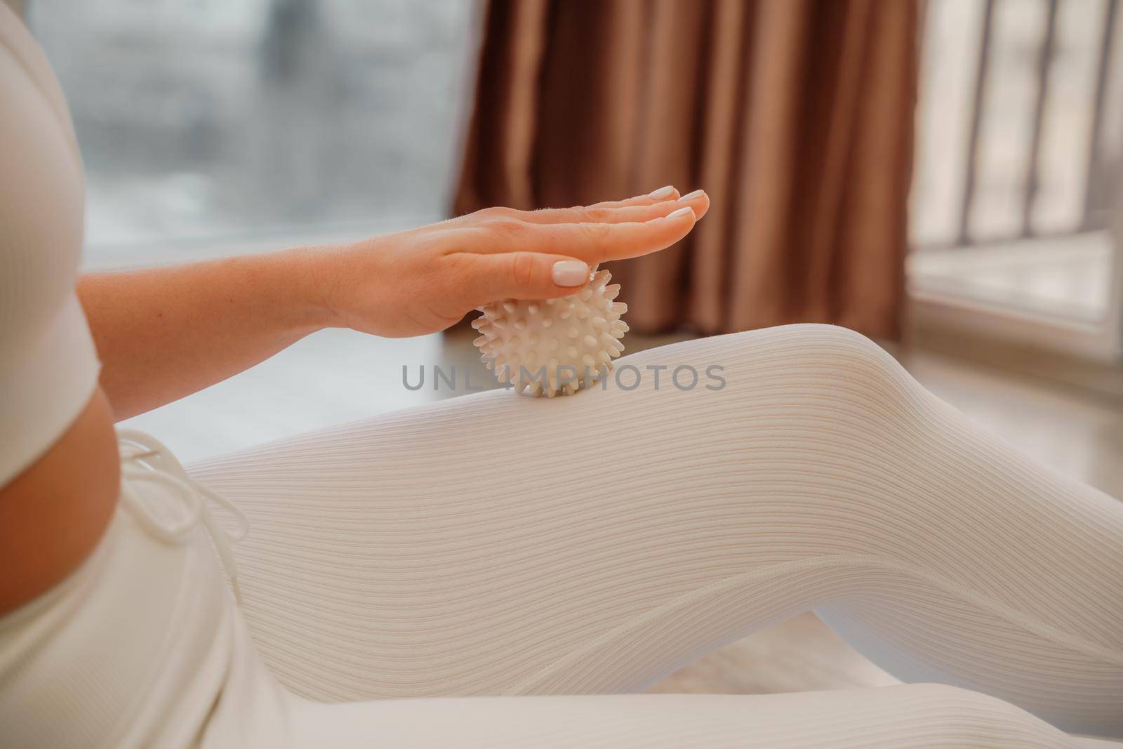 Athletic slim caucasian woman doing thigh self-massage with a massage ball indoors. Self-isolating massage.