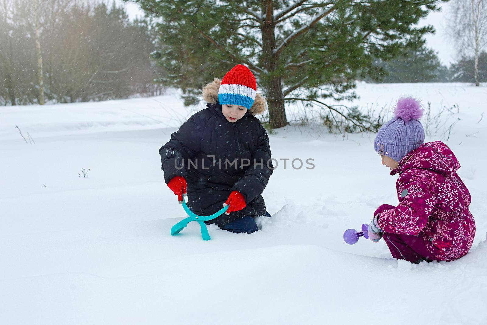 A teenage boy and a little girl outside in a winter park make snowballs with plastic sculpting tools. copy space