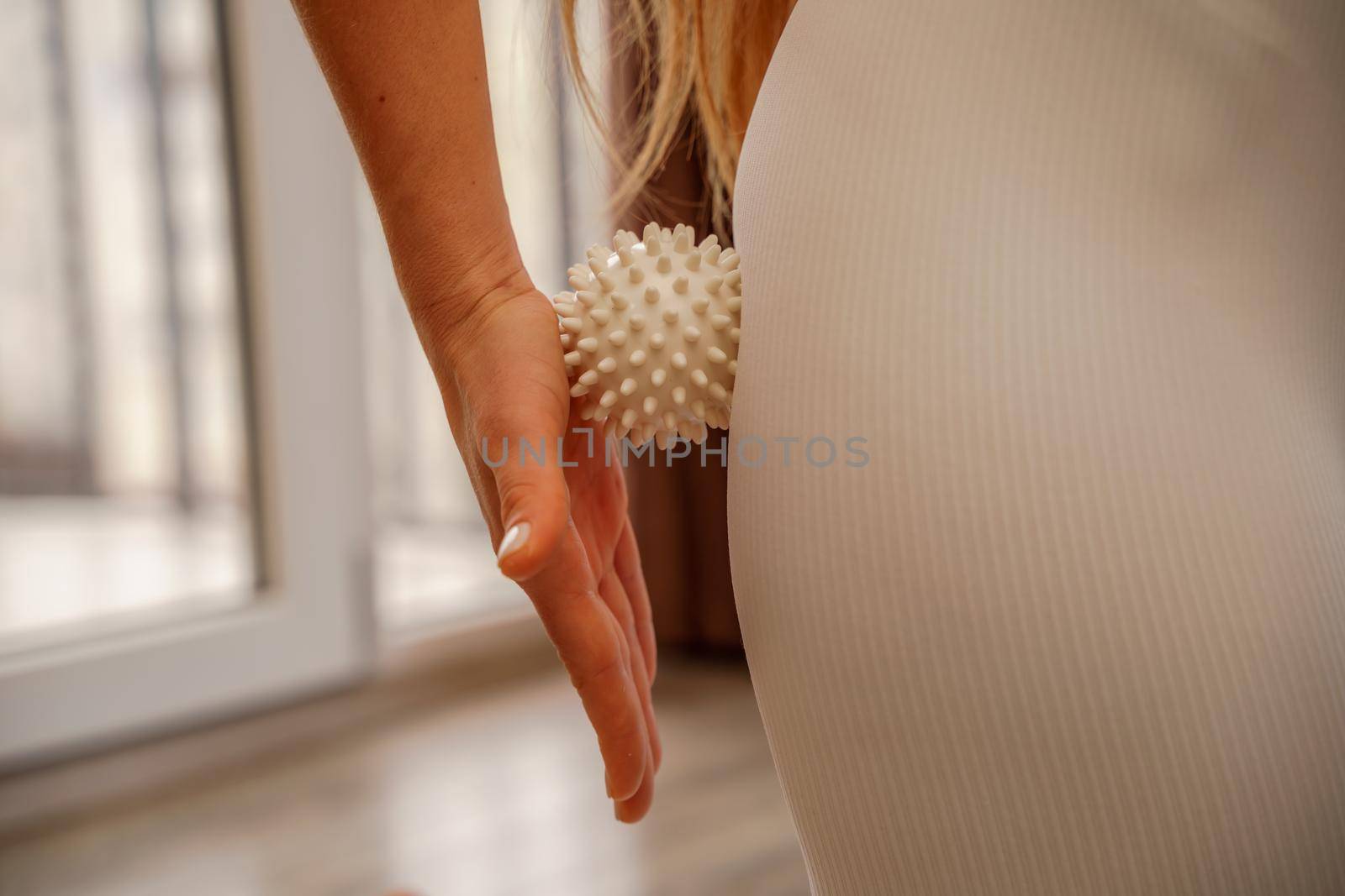 Athletic slim caucasian woman doing thigh self-massage with a massage ball indoors. Self-isolating massage by Matiunina