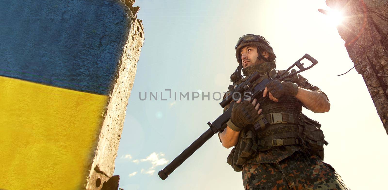 Ukrainian Soldier military in the war with a weapon in his hands. The flag of Ukraine is painted on a brick wall. Relations between Ukraine and Russia.