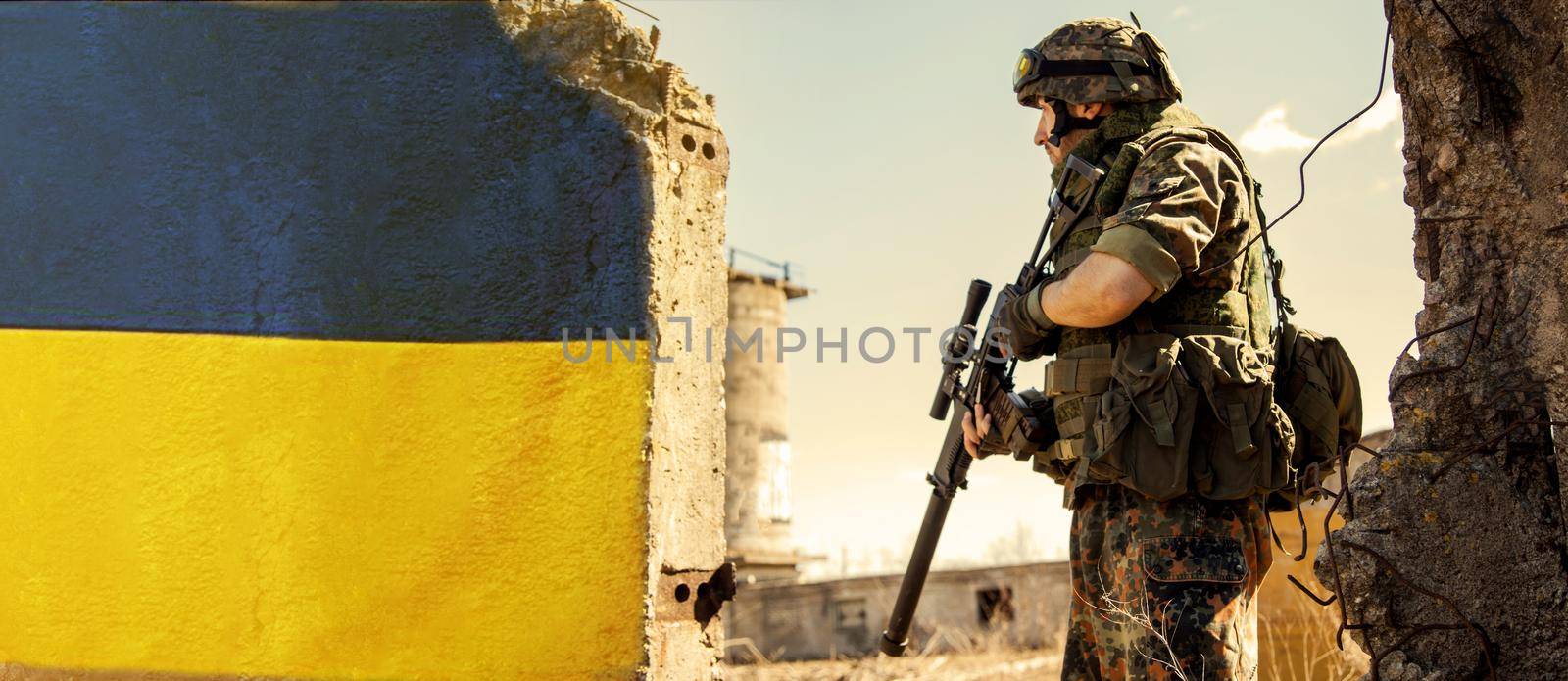 Ukrainian Soldier military in the war with a weapon in his hands. The flag of Ukraine is painted on a brick wall. Relations between Ukraine and Russia.