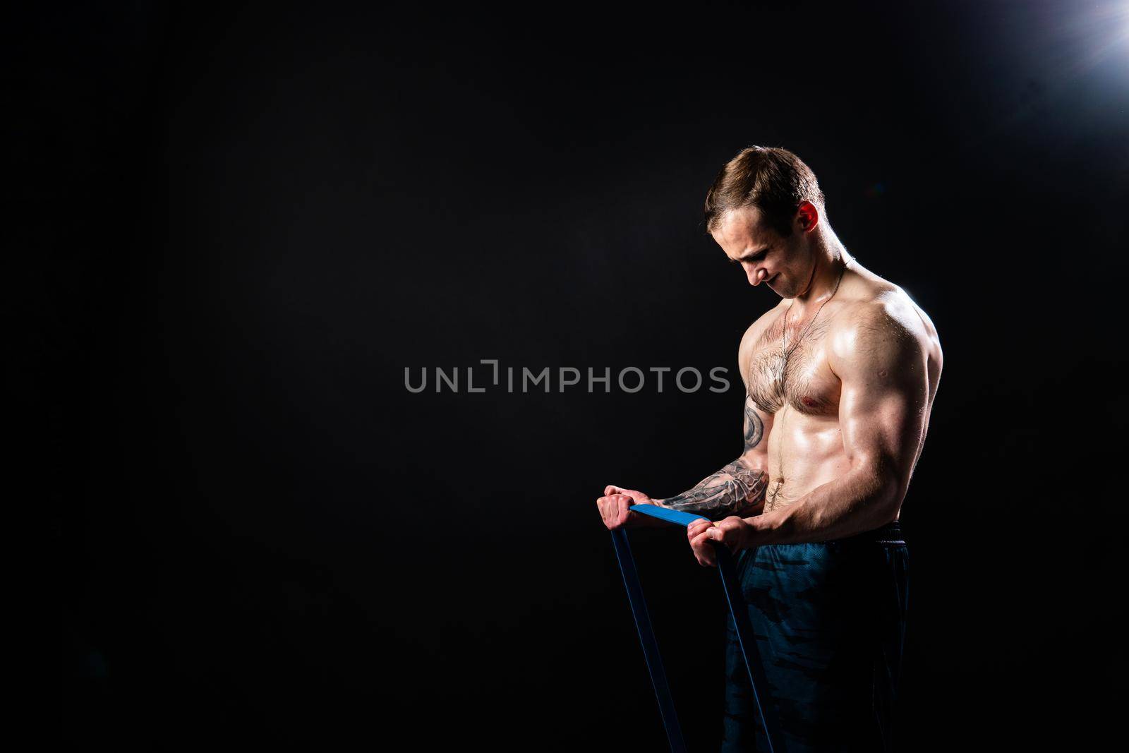 Man on black background keeps dumbbells pumped up in fitness chest black, body hold hand, male people fit With a ribbon in hand, the fitness gum is black