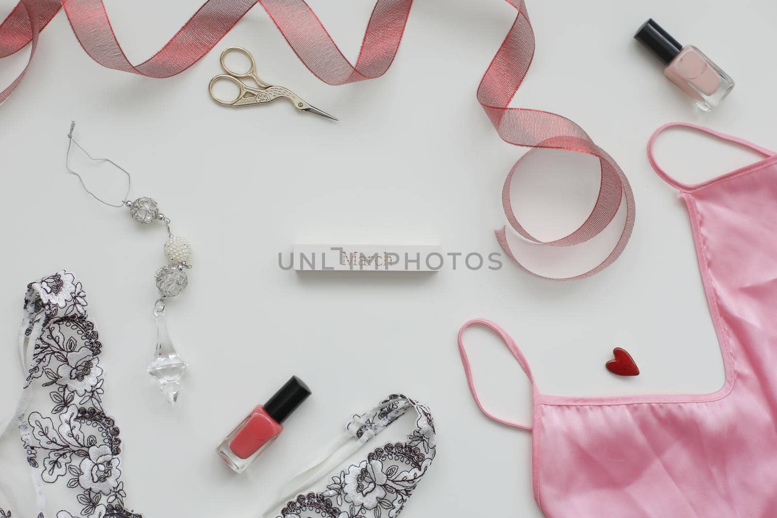 Concept Women's Day, March 8. Female underwear with a red ribbon and cosmetics on white background. Styled flat lay, top view, copy space