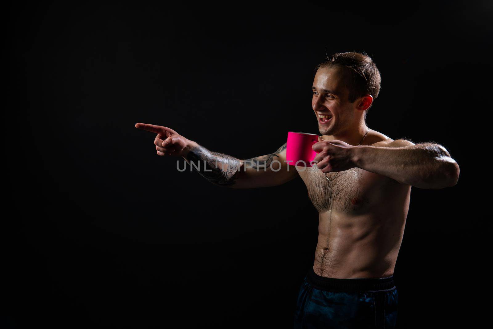 Man on black background keeps dumbbells pumped up in fitness bodybuilding chest black, arm training man bodybuilder hand, male lifestyle. Attractive sportive adult, human fit In the athlete's pink cup he smiles