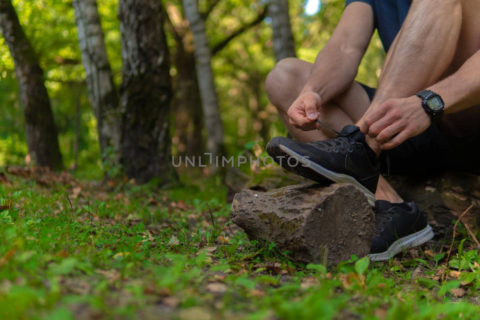 Man tying his shoelaces in the park outdoors, around the forest, oak trees green grass young enduring athletic athlete. active sport forest, lifestyle trail endurance legs marathon, woods Adult energy runners stretches