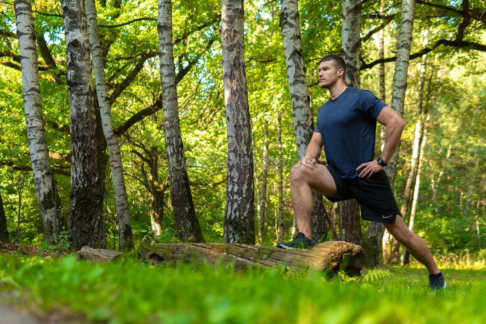 A young enduring athletic athlete is doing stretching in the forest outdoors, around the forest, oak trees.healthy sport forest, workout jogger training person marathon, man. Autumn leisure feet stretches