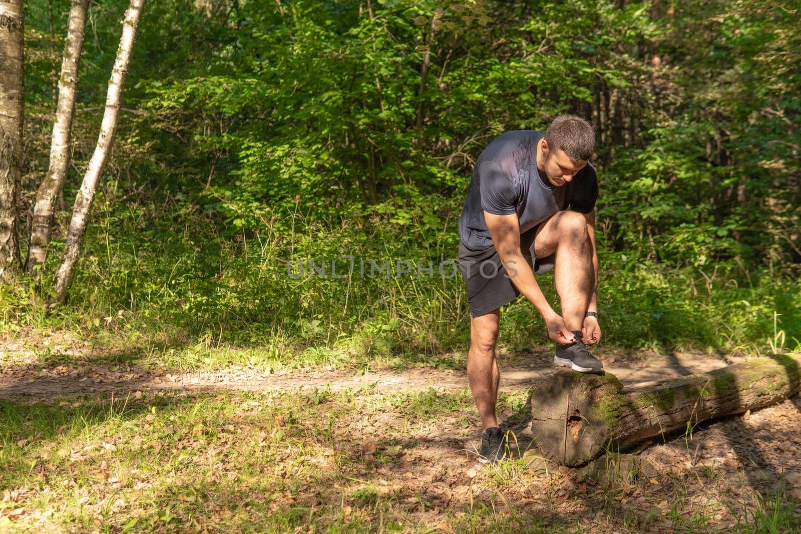 The sportsman is tying the laces of his legs in sneakers close up the athlete runs in the park outdoors, around the forest, oak trees green grass young enduring athletic athlete active exercise, jogger wellness male, woods running, feet stretches