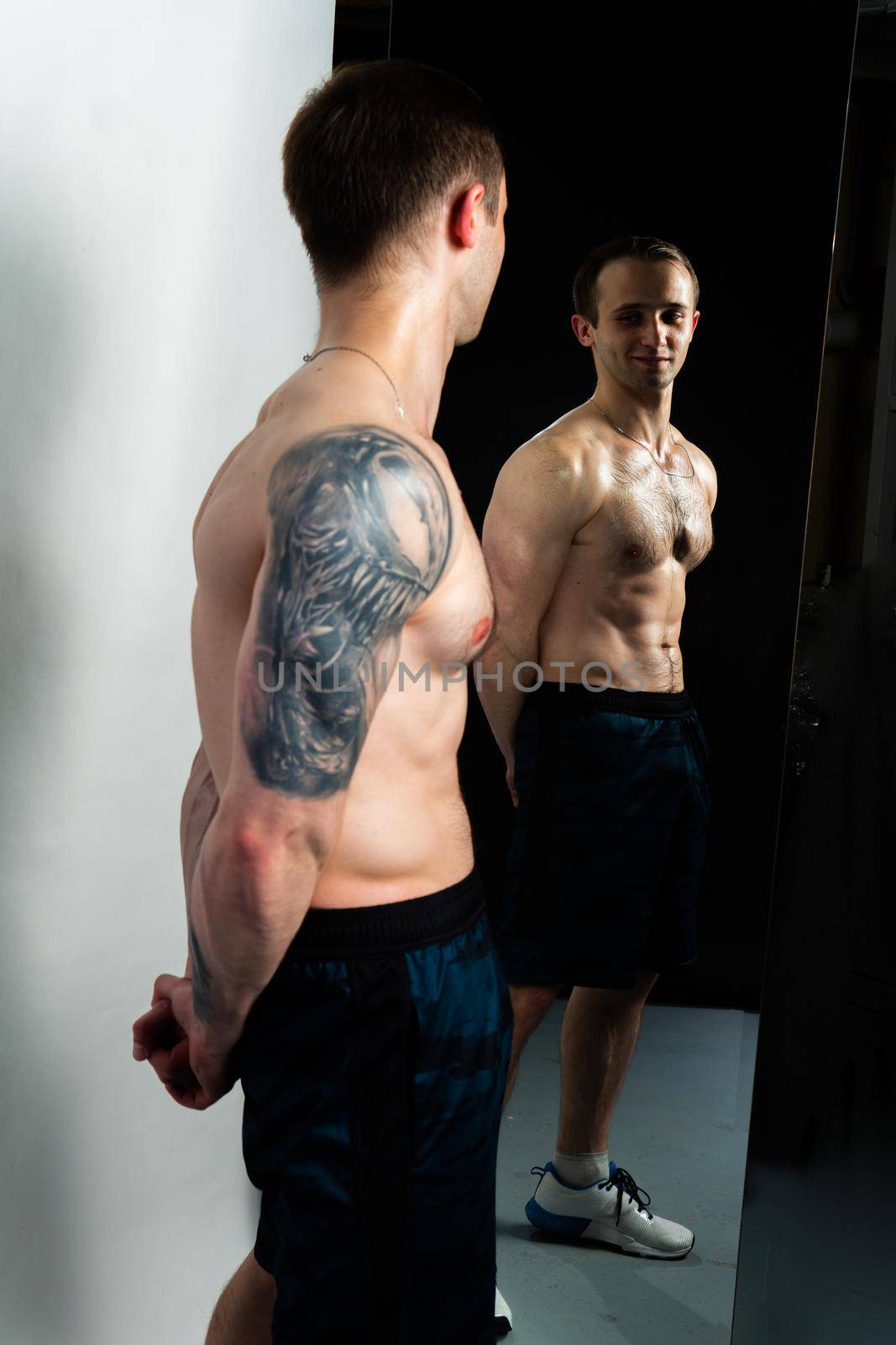 Man on black background keeps dumbbells pumped up in fitness bodybuilding training hand, shirtless lifestyle. Lift sportive human fit In mirror reflection, the body is pumped up