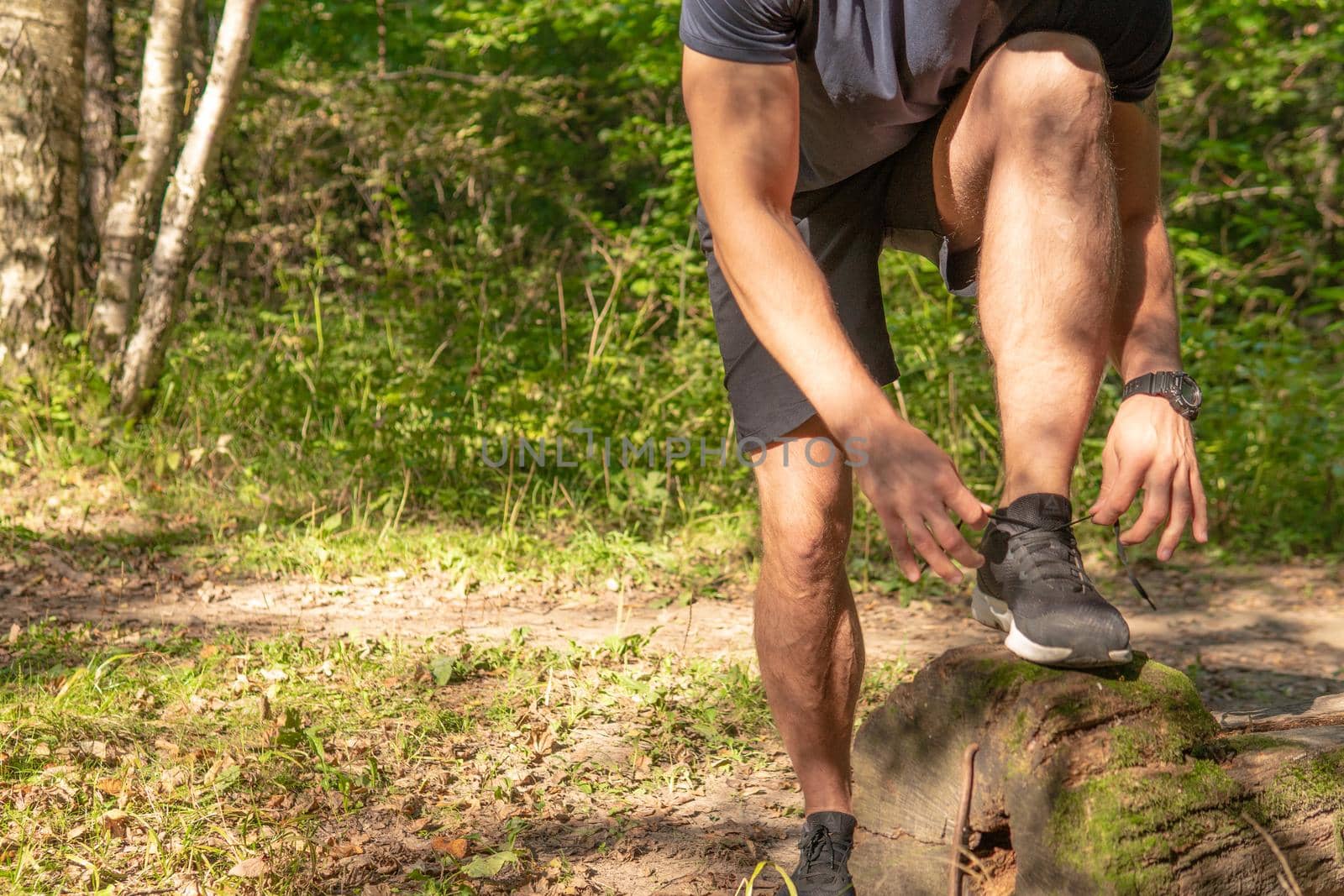 The sportsman is tying the laces of his legs in sneakers close up the athlete runs in the park outdoors, around the forest, oak trees green grass young enduring athletic athlete run sport exercise, lifestyle outdoor young person male, jogging energy cross, distance stretches