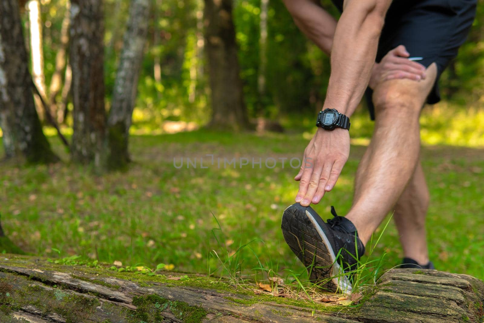A young enduring athletic athlete is doing stretching in the forest outdoors, around the forest, oak trees.active runner forest, lifestyle training wellness motion, jogging wellbeing. Adult body spring, feet stretches