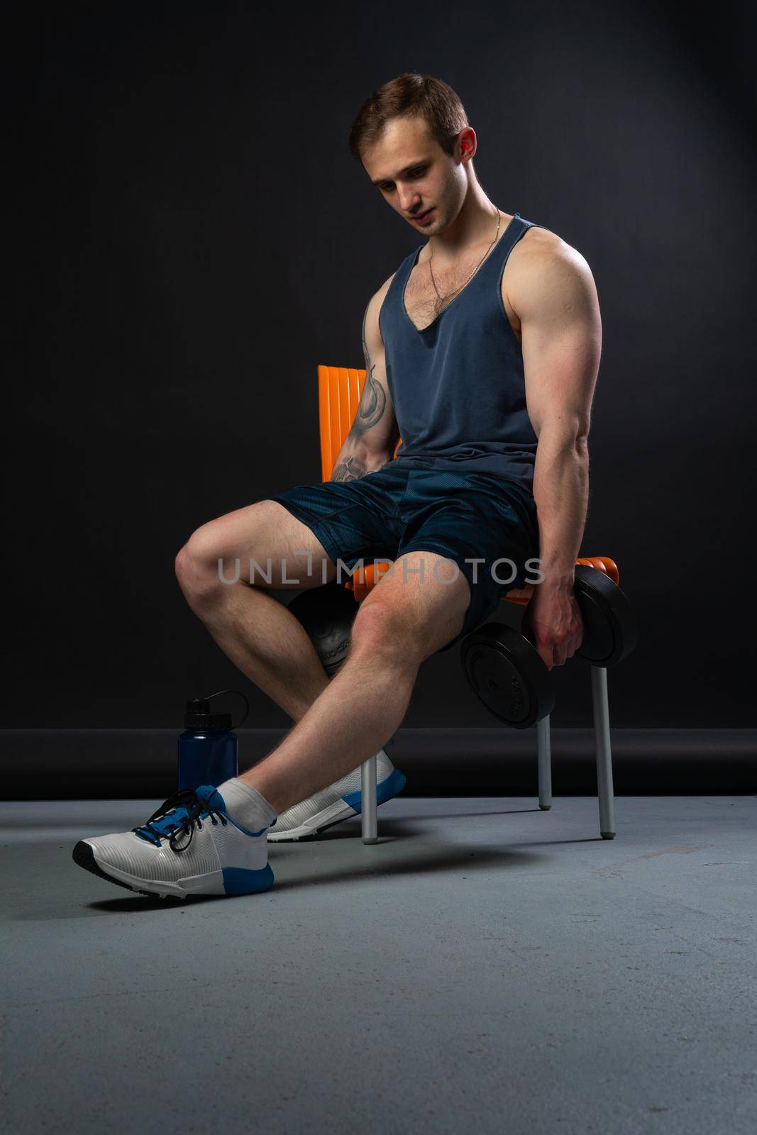 Man on black background keeps dumbbells pumped up in fitness bodybuilding chest torso, arm weight strong healthy Young guy fit sitting on a chair resting after a workout