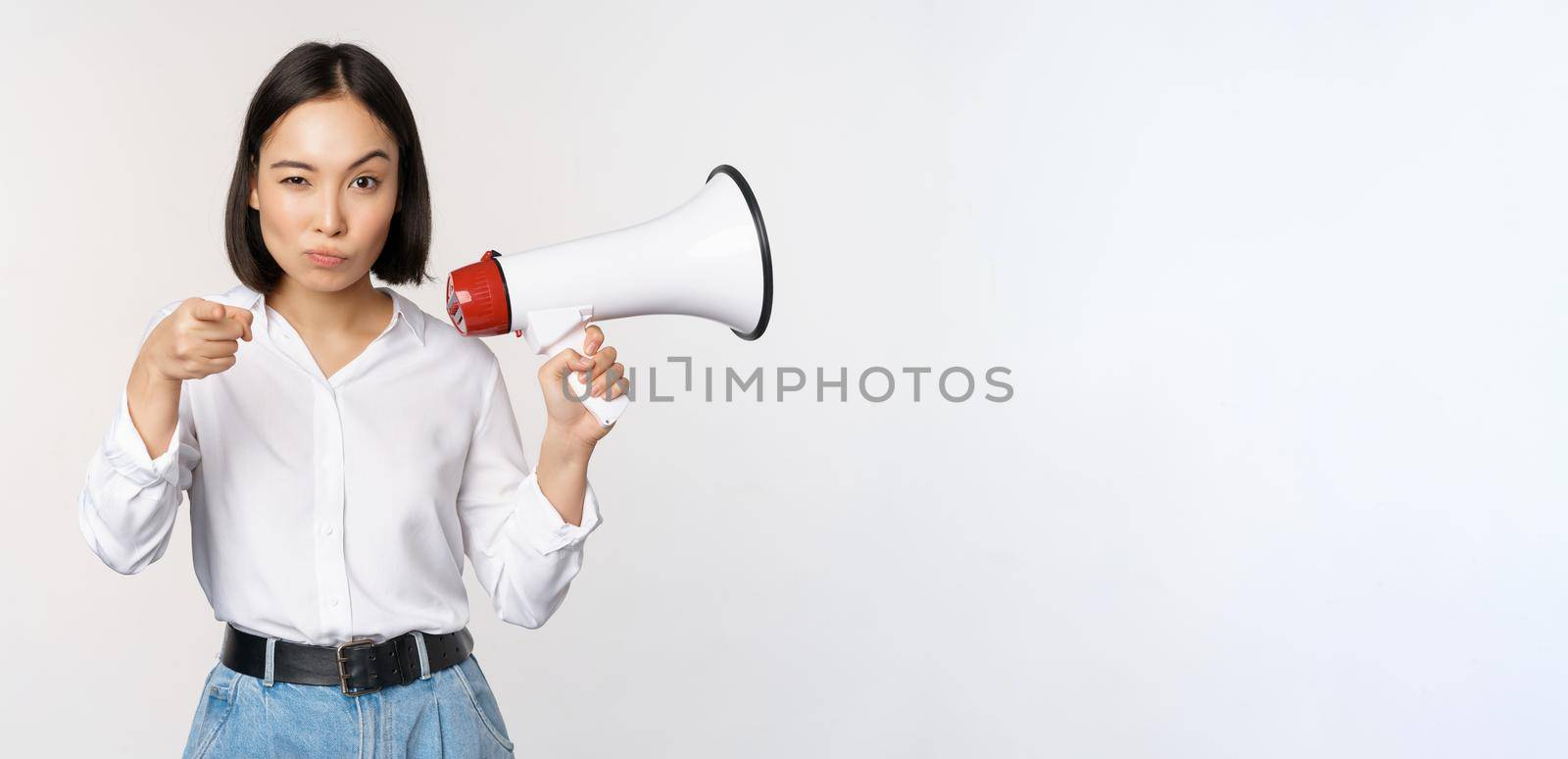 Image of modern asian woman with megaphone, pointing at you camera, making announcement, white background.
