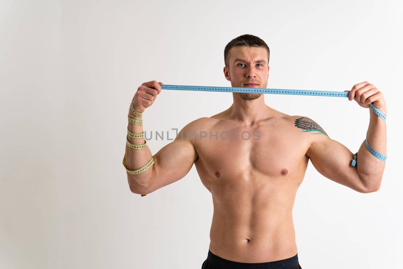 A man measures the waist of a metre and poses against a white background isolated young muscular bodybuilder Measure beautiful caucasian sport attractive tape