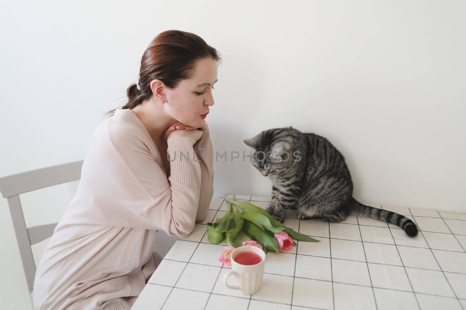 young woman and her cat smelling fresh pink tulips in the morning at home