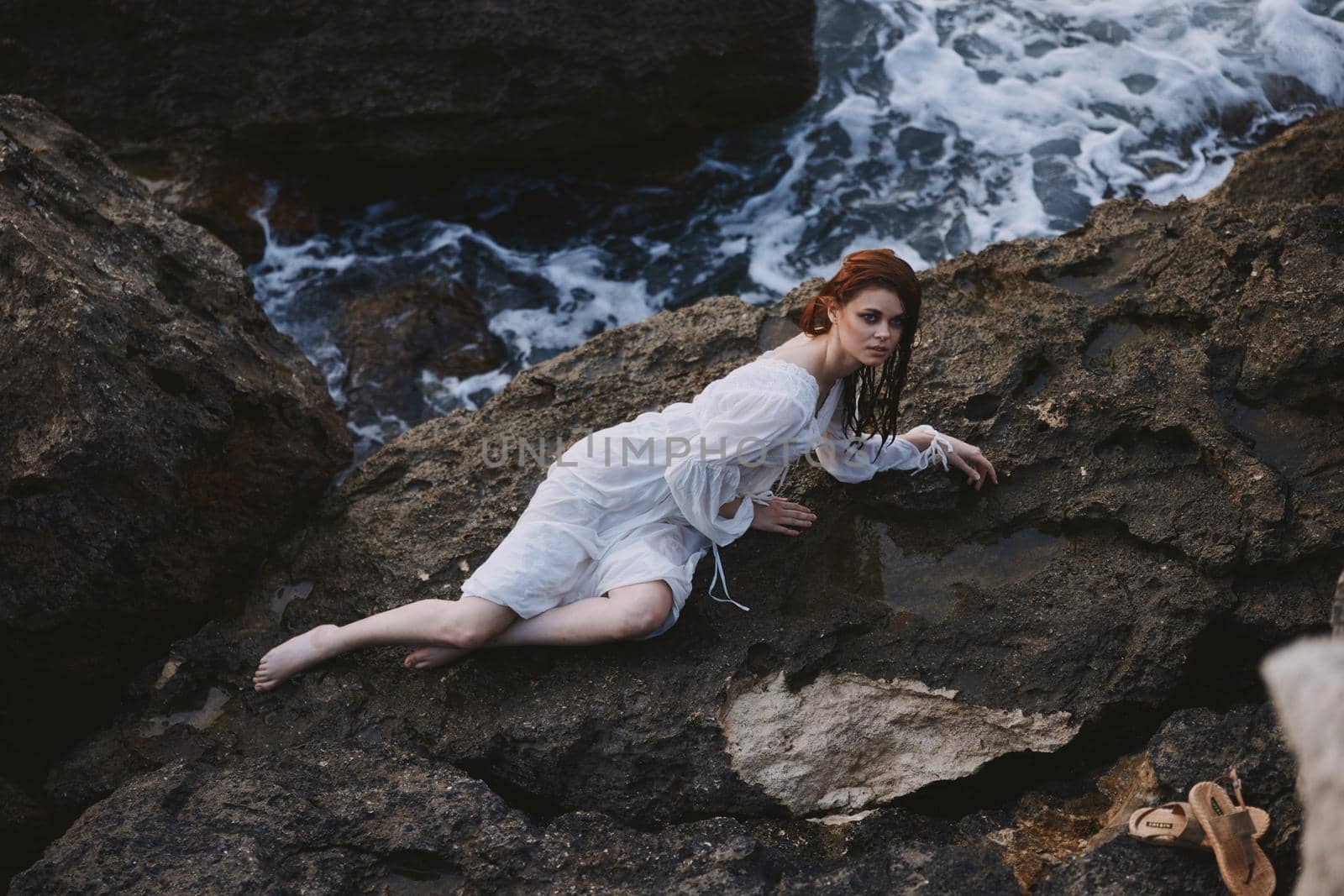 beautiful young woman in long white dress wet hair lying on a rocky cliff unaltered. High quality photo