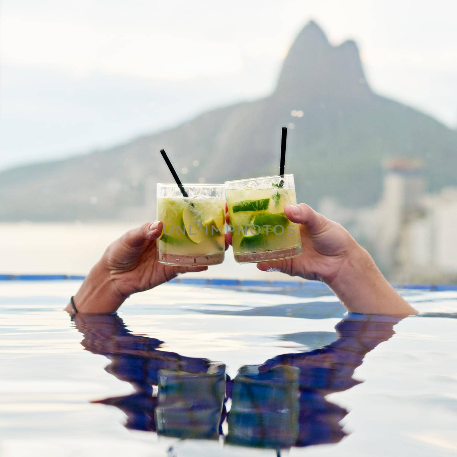 Heres to a wonderful view. Cropped shot of two people toasting in a pool with a view. by YuriArcurs