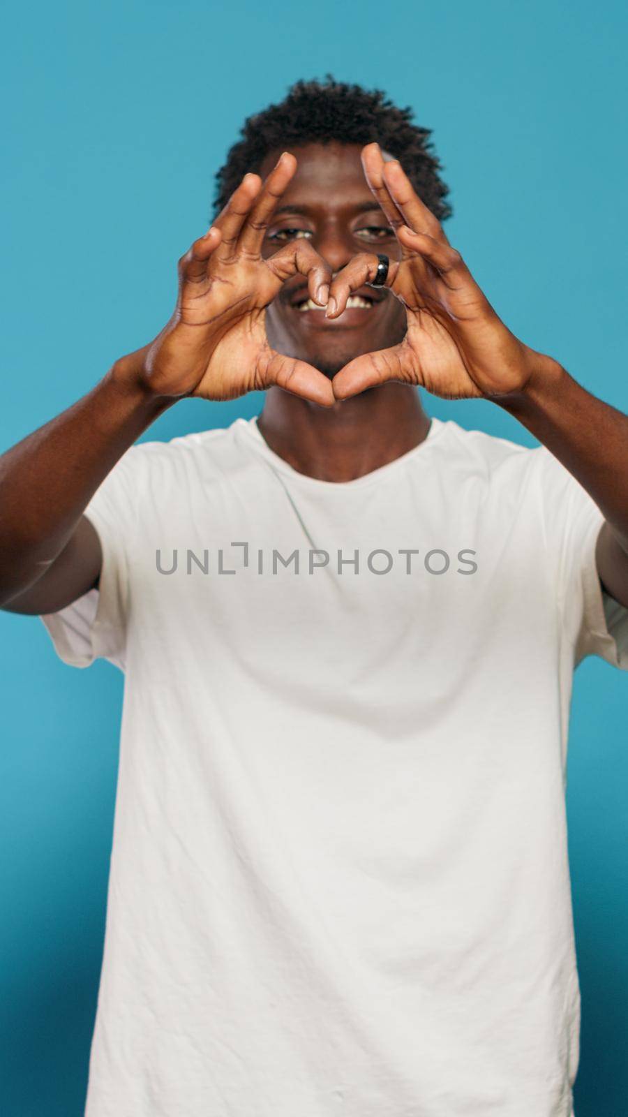 Joyful man doing heart symbol with hands while looking at camera by DCStudio