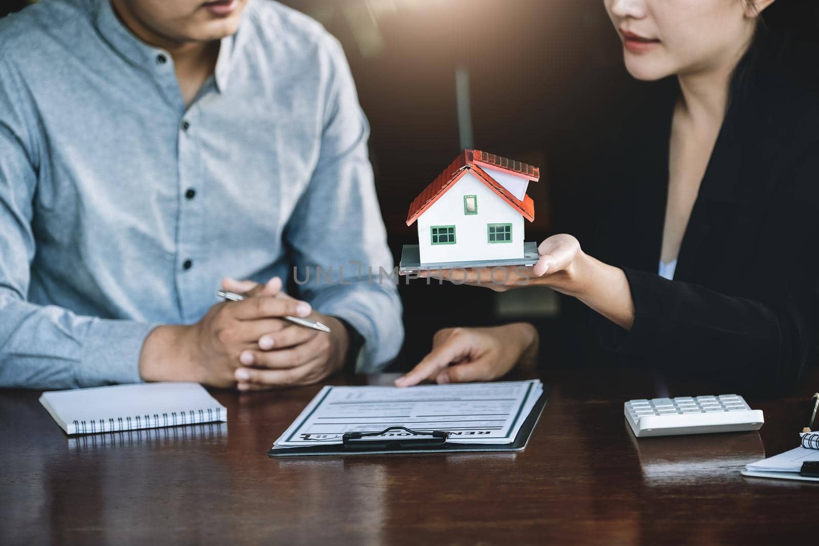 Concept of signing loan agreements, refinancing, buying and selling houses and land, focusing on model houses. A real estate agent is pointing to contract documents for male clients to Buy a dwelling