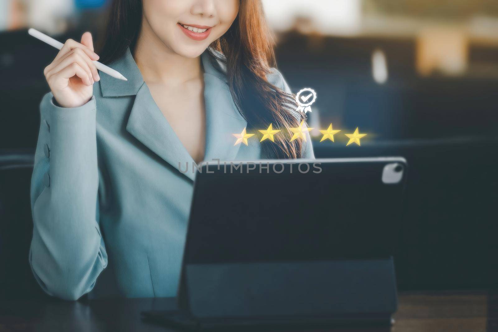 A female entrepreneur or businesswoman showing a smiling face while operating a computer tablet working on a wooden table. by Manastrong