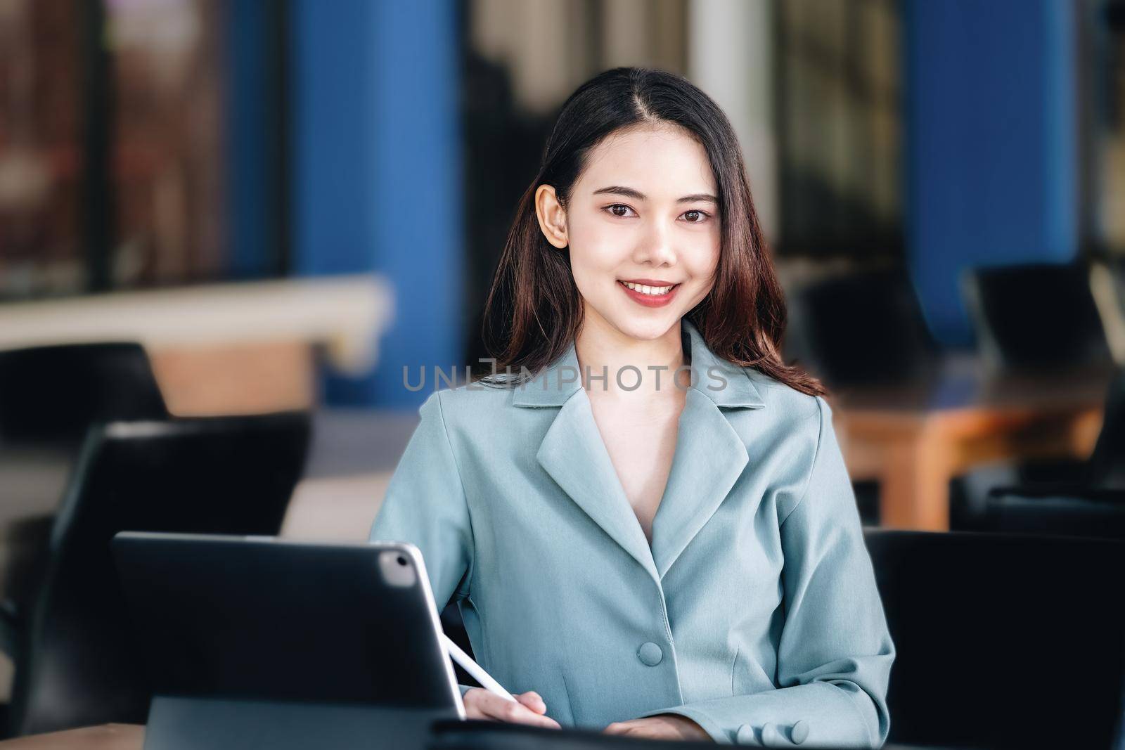 A female entrepreneur or businesswoman showing a smiling face while operating a computer tablet working on a wooden table