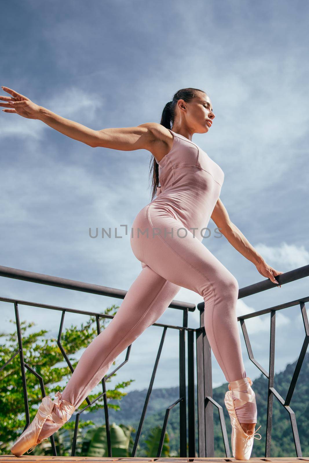 Young fit ballerina in pink pointes stretching and standing on toes in warm sunrise against blue sky. Beautiful ballerina dancing in ballet shoes in outdoor. Beauty fasion. Power, wellbeing concept.