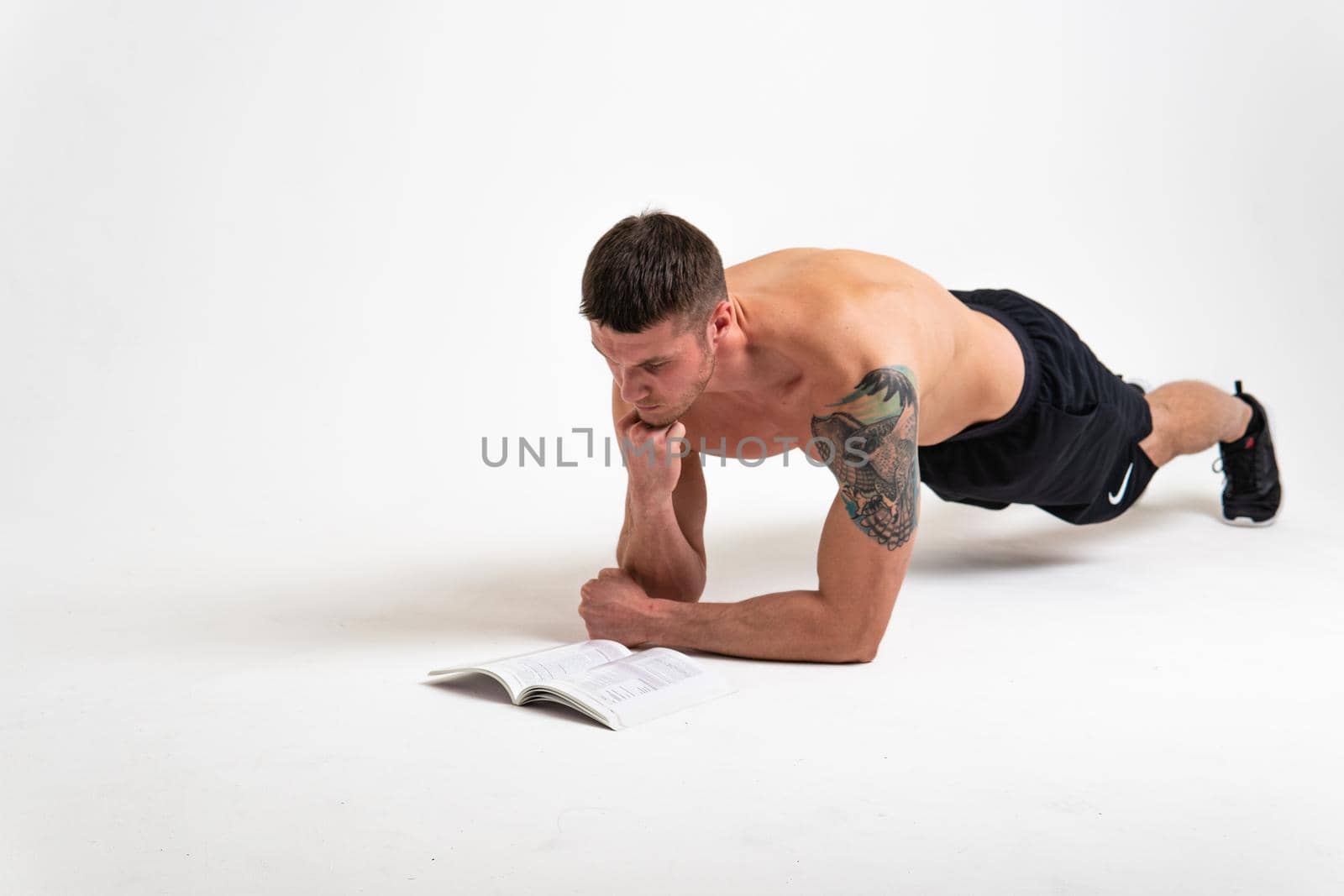 Bodybuilder reads the book on a white background isolated at the bottom of his head on his hands muscle guy adult, sexy sport. ABS holding, vision tan