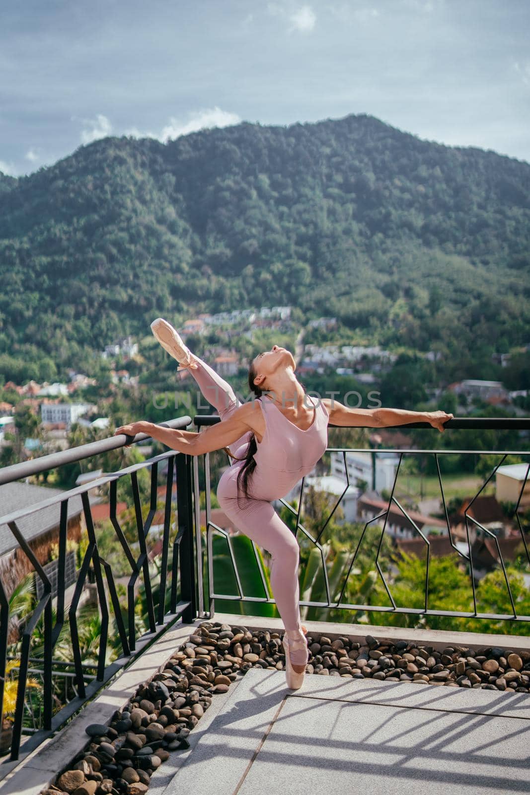 Young fit ballerina in pink pointes stretching and standing on toes in warm sunrise against blue sky. Beautiful ballerina dancing in ballet shoes in outdoor. Beauty and wellbeing concept.