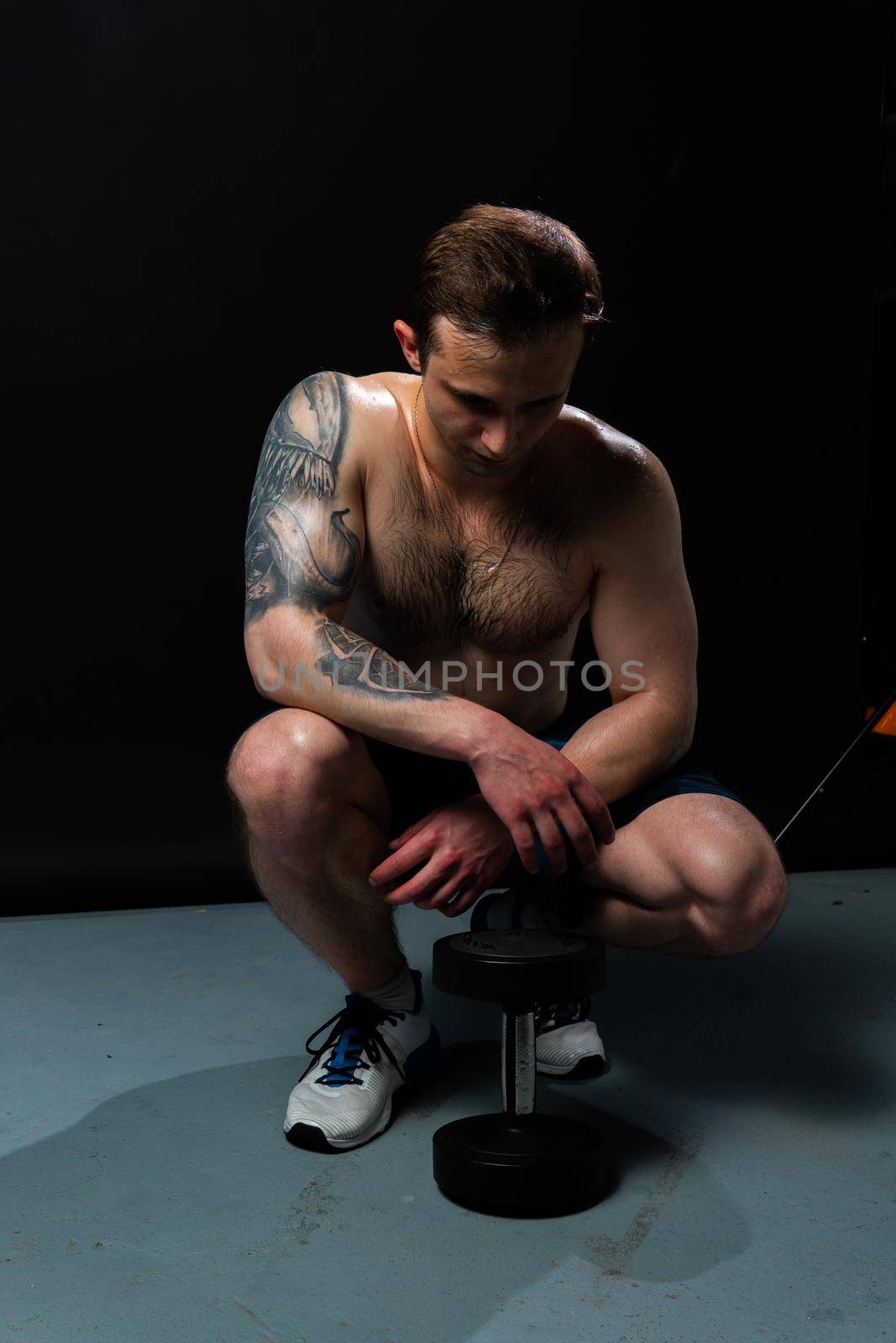 Man on black background keeps dumbbells pumped up in fitness bodybuilding biceps black, muscular bodybuilder heavy, person lifestyle. Attractive adult, gym fit View from the bottom up good press beautiful muscles hairy chest charisma