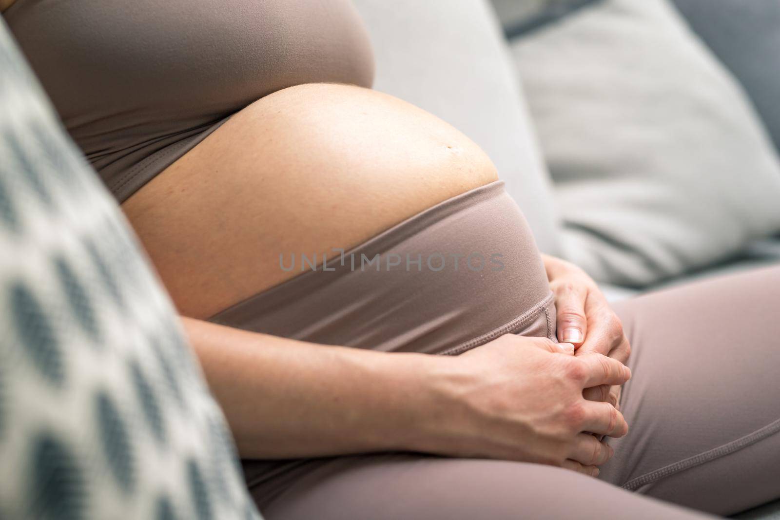 Pregnant woman belly. Pregnancy Concept. Pregnant tummy close up. Detail of pregnant woman relaxing on comfortable sofa at home
