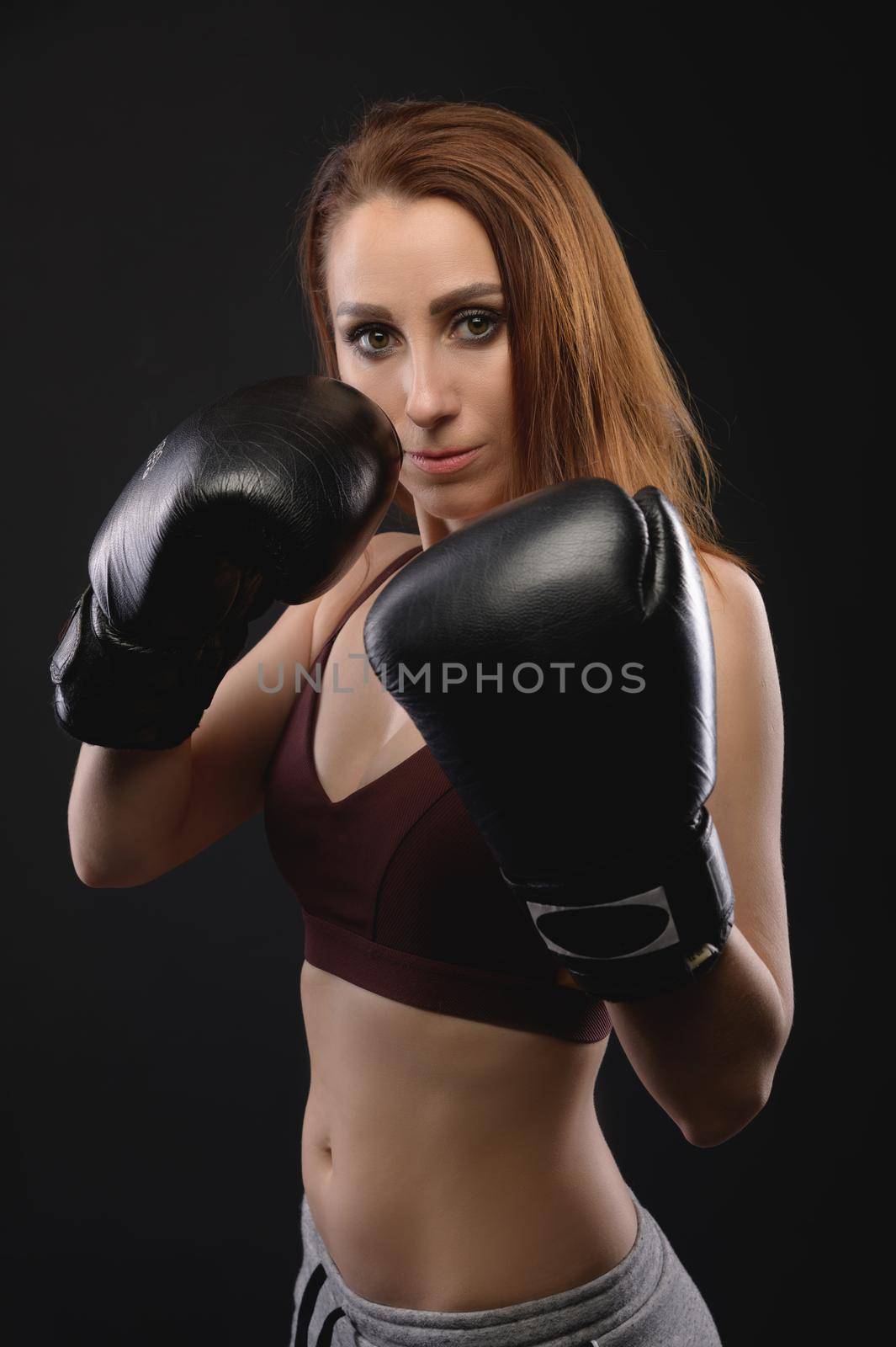 Strong and strict caucasian woman fighter in sportswear and boxing gloves on a black background. Feminism and combat sports.