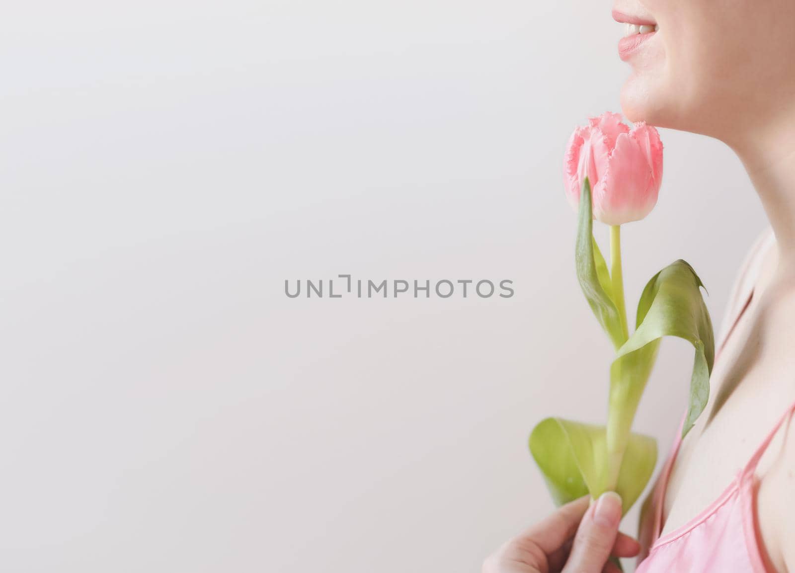 spring portrait of a young woman with pink fresh tulip on white background with copyspace.