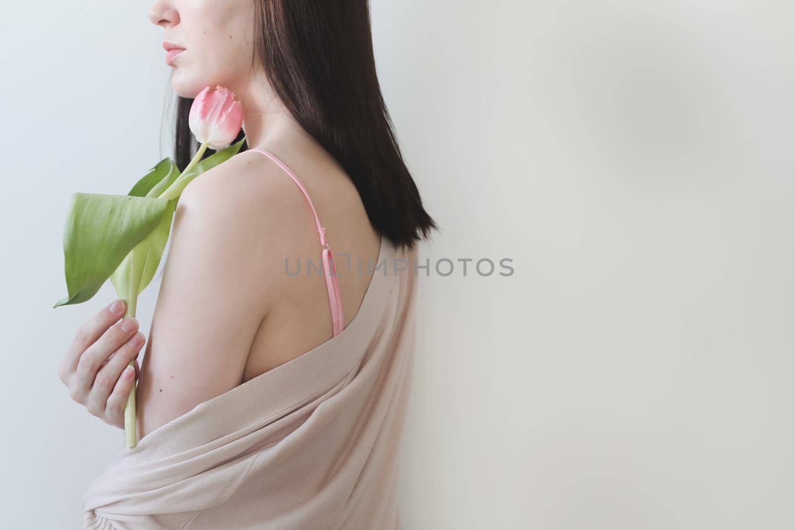 spring portrait of a young woman with pink fresh tulip on white background with copyspace.