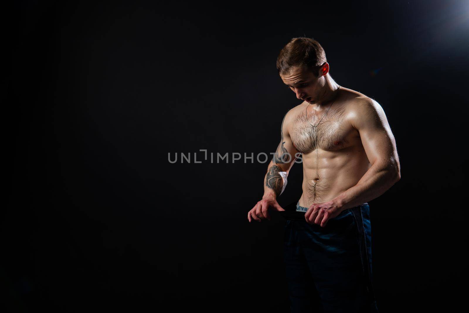 Man on black background keeps dumbbells pumped up in fitness active sport, body muscular strong bodybuilder shirtless lifestyle. Young one fit Look at the press and measures the size of pants for weight loss