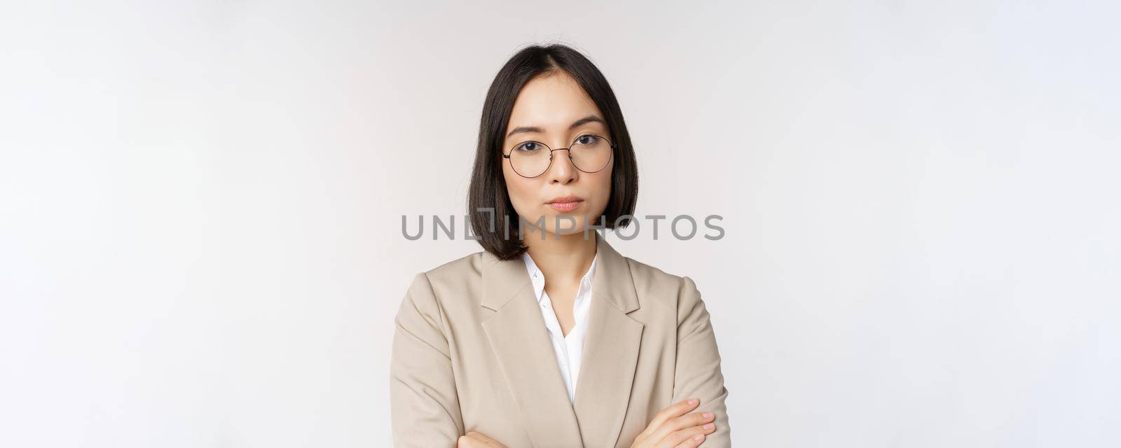 Professional asian businesswoman in glasses, looking confident at camera, standing in power pose against white background.