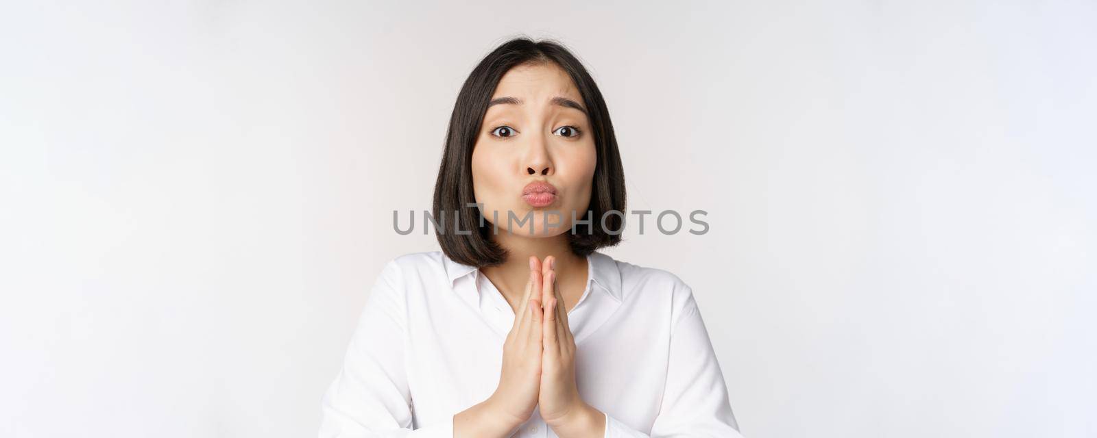 Cute asian woman begging, say please, asking for favour, need help, standing with coy face against white background.