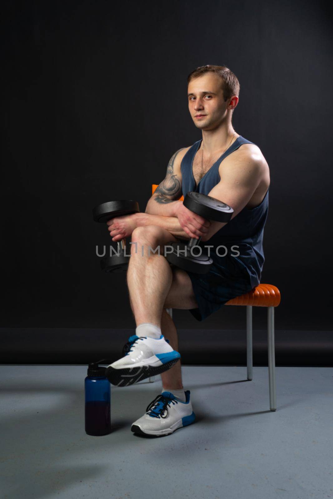 Man on black background keeps dumbbells pumped up in fitness active sexy torso, training hold hand, metal, human fit sitting on a chair resting after a workout