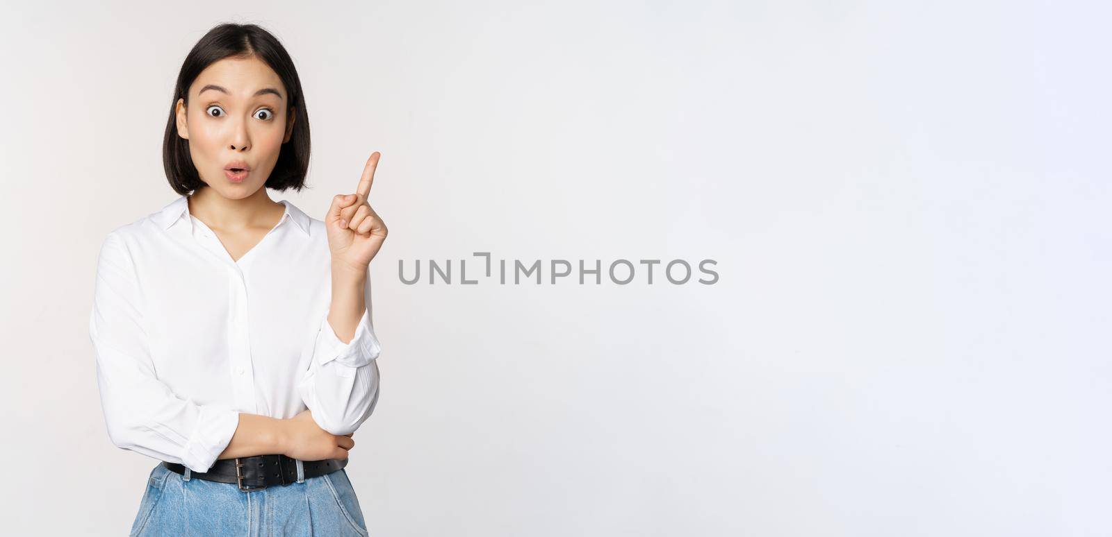 Eureka. Young smart asian girl has an idea, raising finger up, sharing her plan, pointing on top, standing over white background.