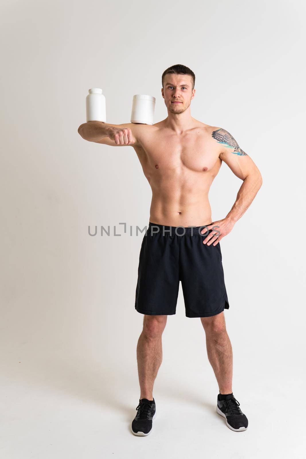 Fitness protein jars white on white background bodybuilder powder strong high pain injury, cramp caucasian young adult, muscular expression. Hold neck therapy, back suffer attractive