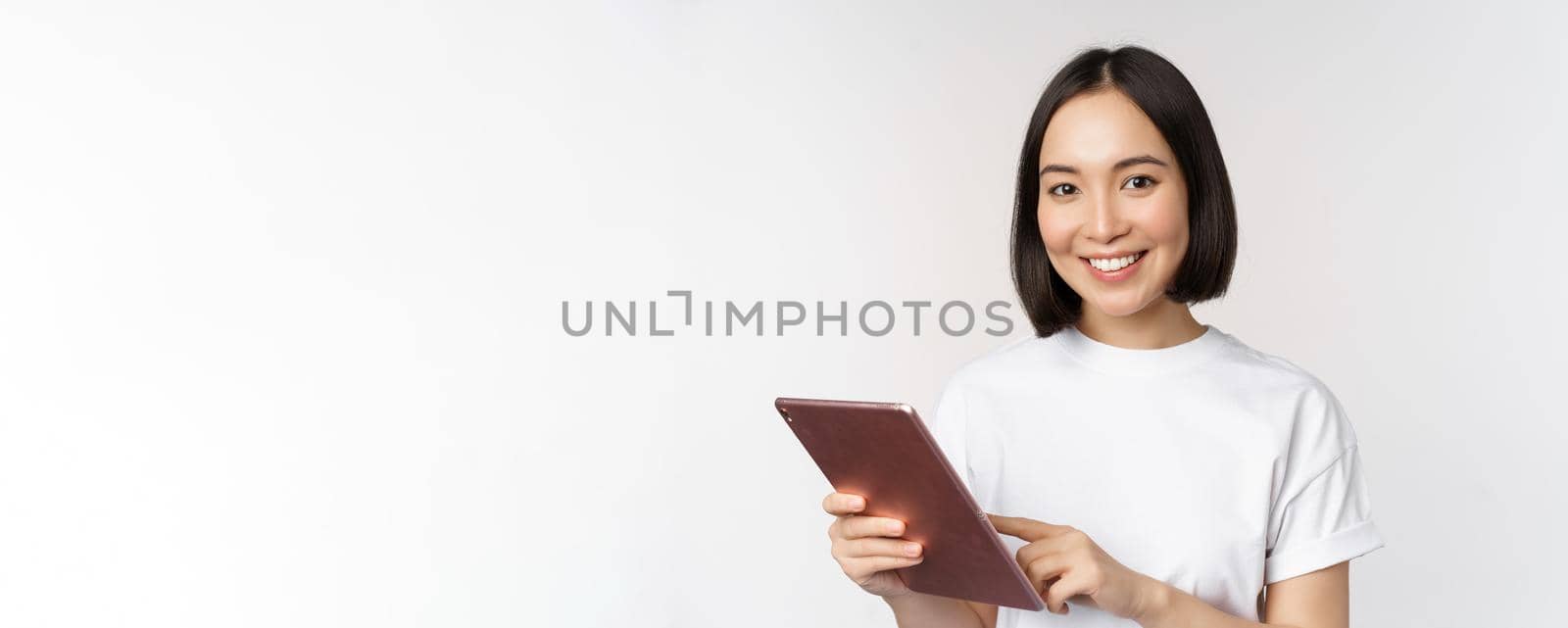 Asian girl using digital tablet, working with gadget, shopping online, standing over white background by Benzoix