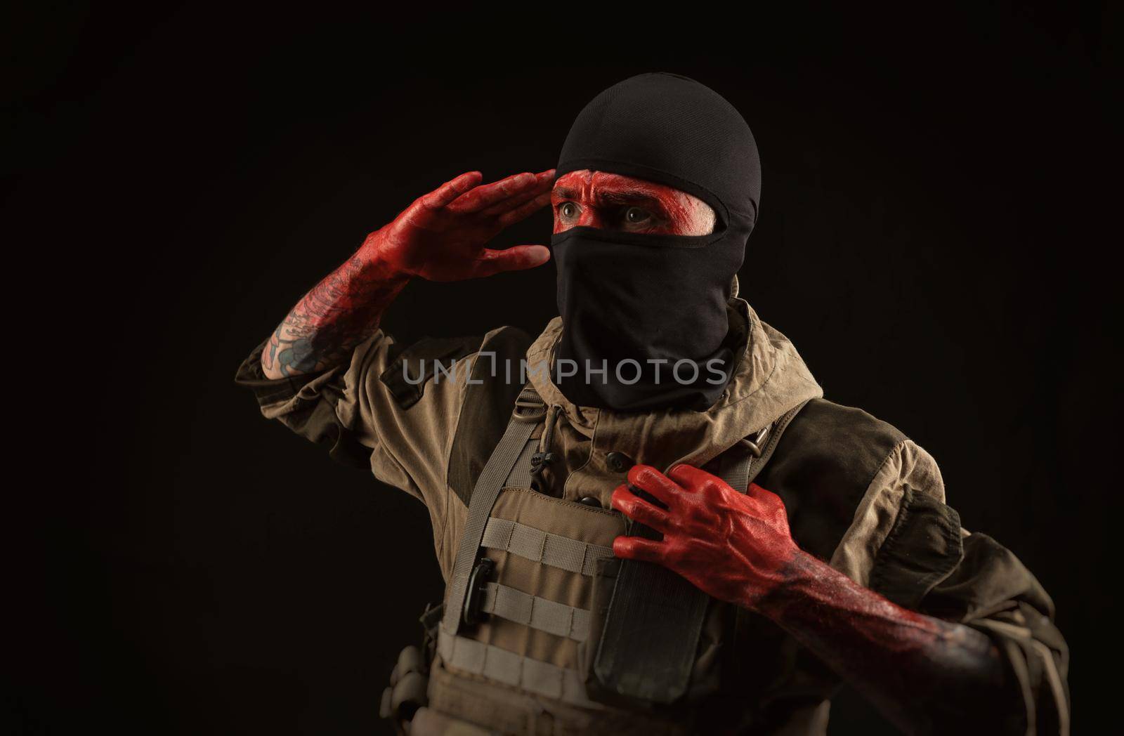 the photo of a man in a military uniform and balaclava with a bloody face and hands up to the elbow in blood on a black background