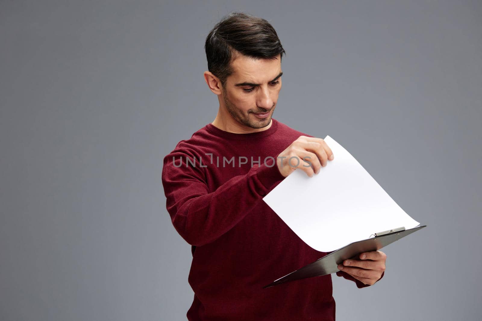 manager looks at the tablet with papers in a red sweater posing Gray background. High quality photo