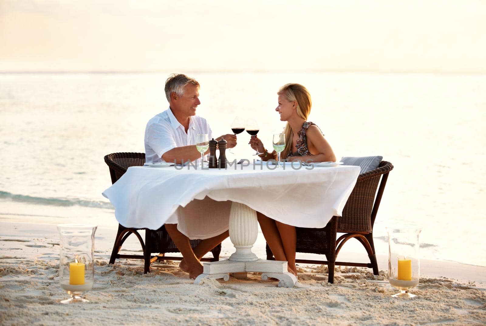 Romantic couple celebrating with wine at the beach. Shot of a mature couple enjoying a romantic dinner on the beach. by YuriArcurs